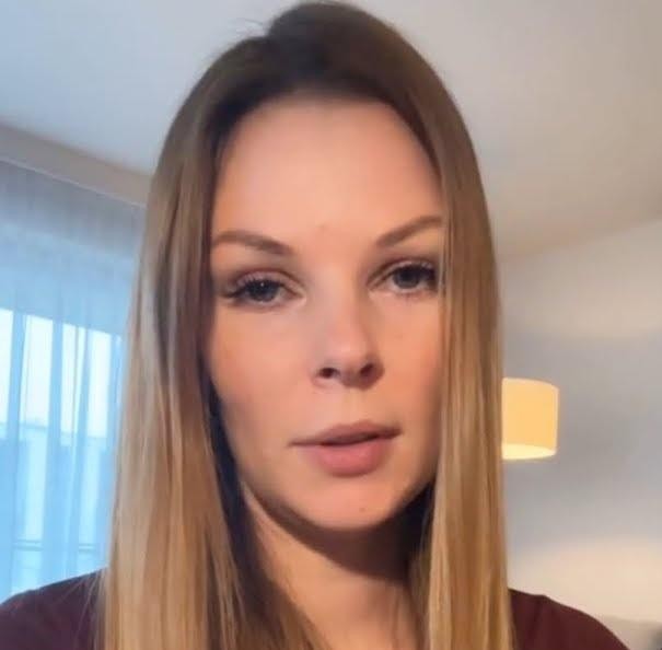 Małgorzata Tomaszewska prowadząca program telewizyjny, ubrana elegancko, z mikrofonem w ręku, na tle studia.