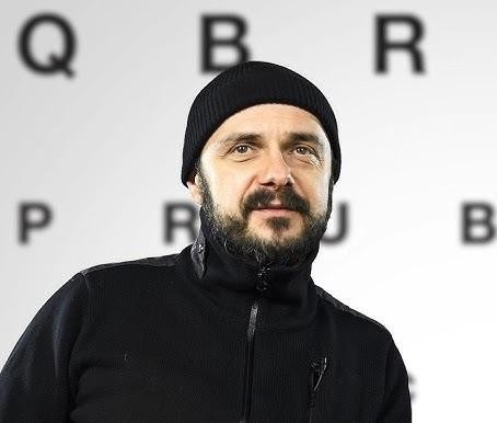Portret Arkadiusza Jakubika z intensywnym spojrzeniem, z rozmytym tłem nawiązującym do jego kariery filmowej i muzycznej.