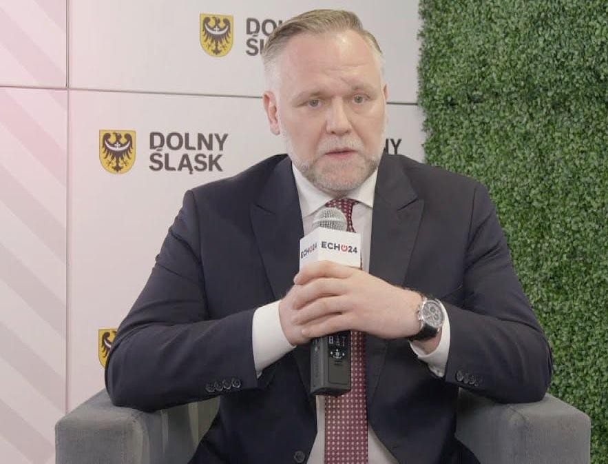 Dawid Jackiewicz przemawiający na wiecu politycznym, z energicznym gestem ręki, w tle zamazany tłum.
