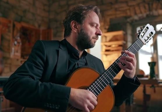Młody Marcin Dylla, student, ćwiczący grę na gitarze klasycznej w sali lekcyjnej akademii muzycznej.