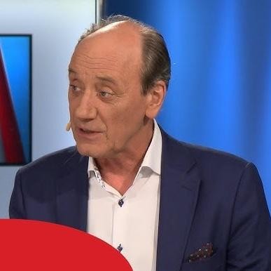 Dariusz Szpakowski komentujący mecz z pasją, z mikrofonem blisko ust, na tle rozmytego stadionu.