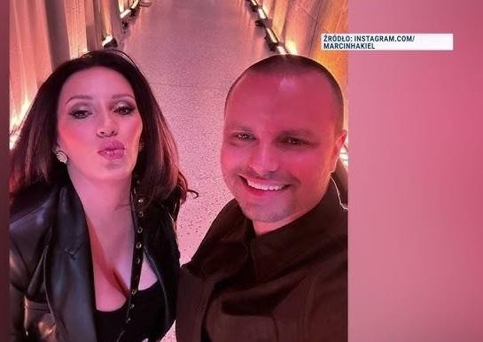 Marcin Hakiel z telefonem, uśmiechnięty, w interakcji z mediami społecznościowymi.