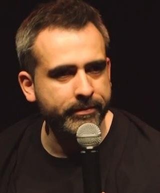 Abelard Giza podczas występu stand-upowego, wchodzący w interakcję z publicznością, gestykulujący i uśmiechnięty.