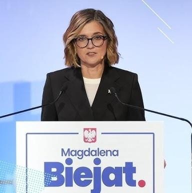 Magdalena Biejat podczas spotkania z wyborcami, uśmiechnięta i serdecznie gestykulująca, otoczona entuzjastycznym tłumem, symbolizująca bliski kontakt z obywatelami.