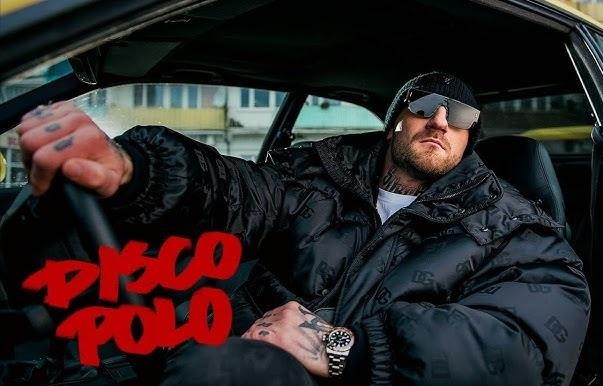 Kizo podczas energicznego występu na scenie, rapujący do mikrofonu, z dynamicznym oświetleniem i rozmazaną publicznością w tle.